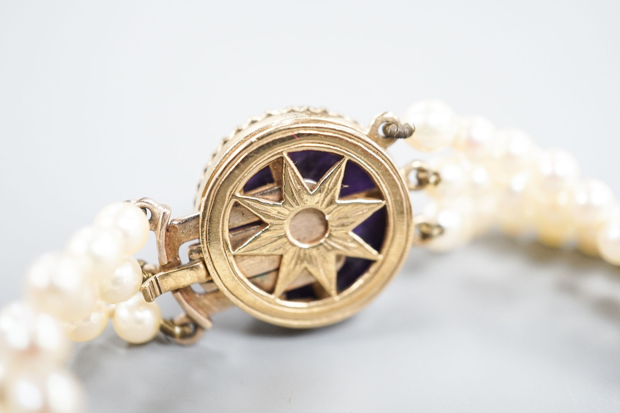 An early 20th century triple strand cultured? pearl bracelet, with rose cut diamond and cabochon amethyst set yellow metal clasp, 17.5cm, gross weight 21 grams.